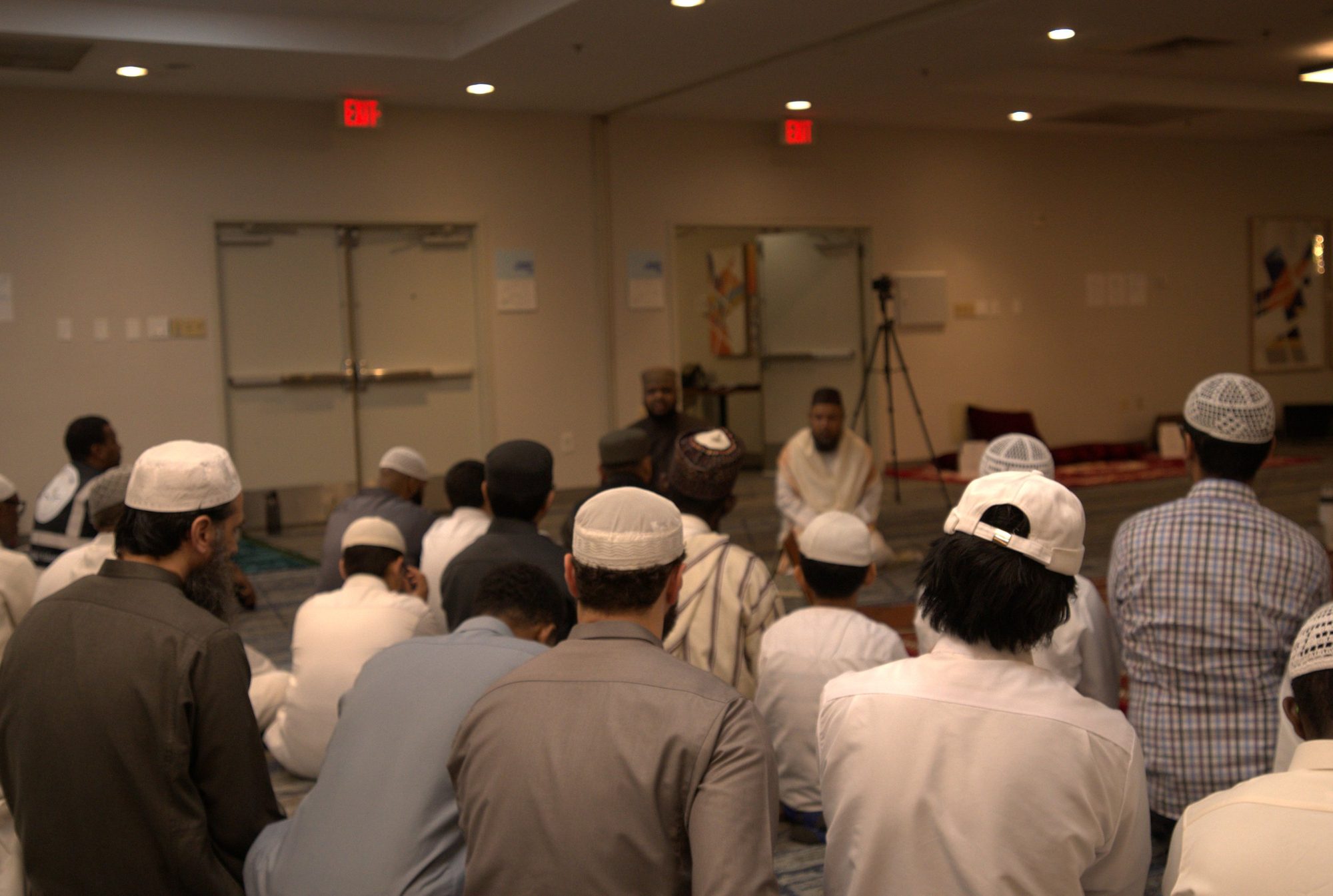 Men seated in rows on the floor facing a speaker at a gathering in the institute's hall