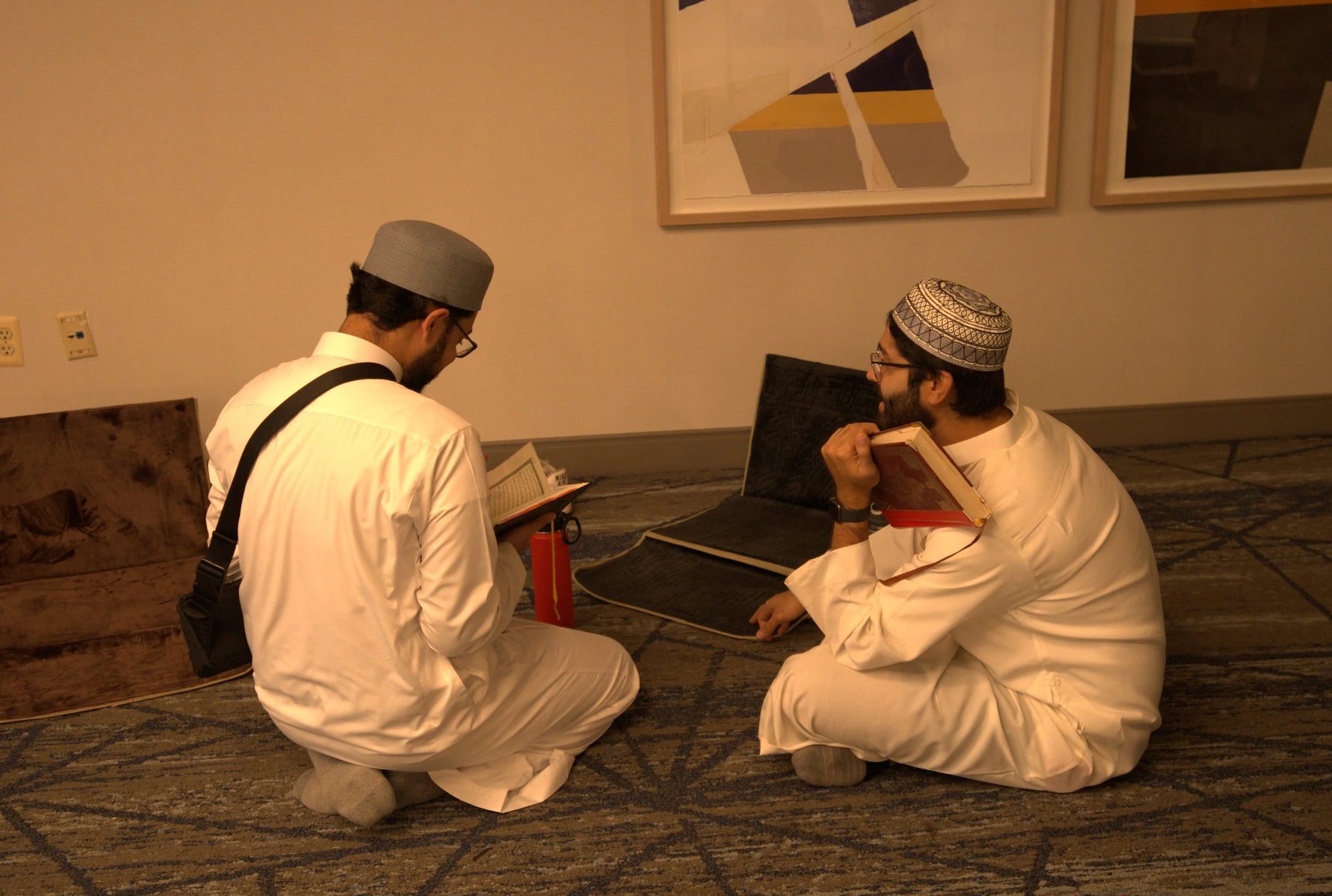 Two young men seated on the floor reciting Qur'an to each other