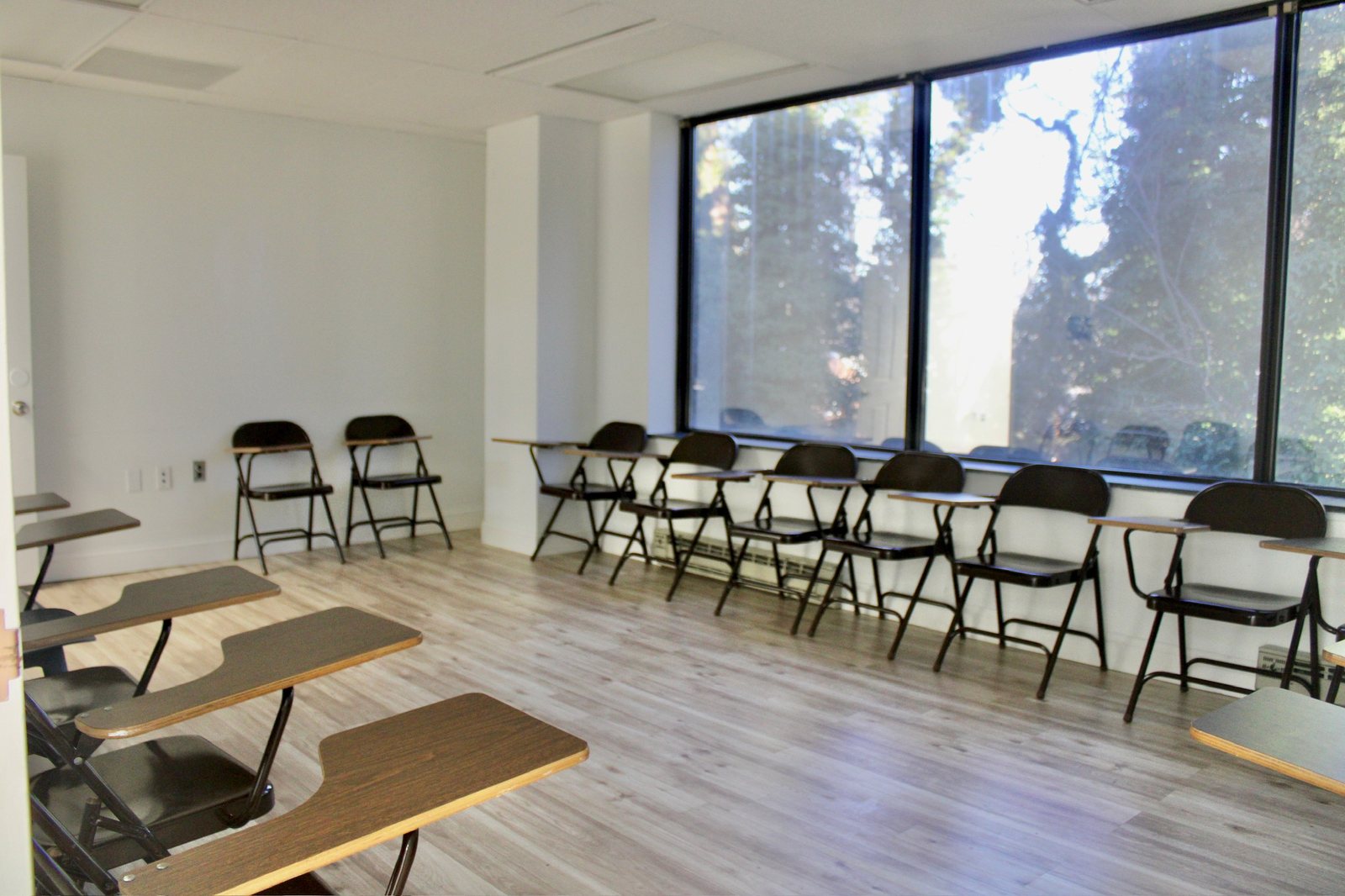 An empty classroom with rows of desk chairs beside large windows