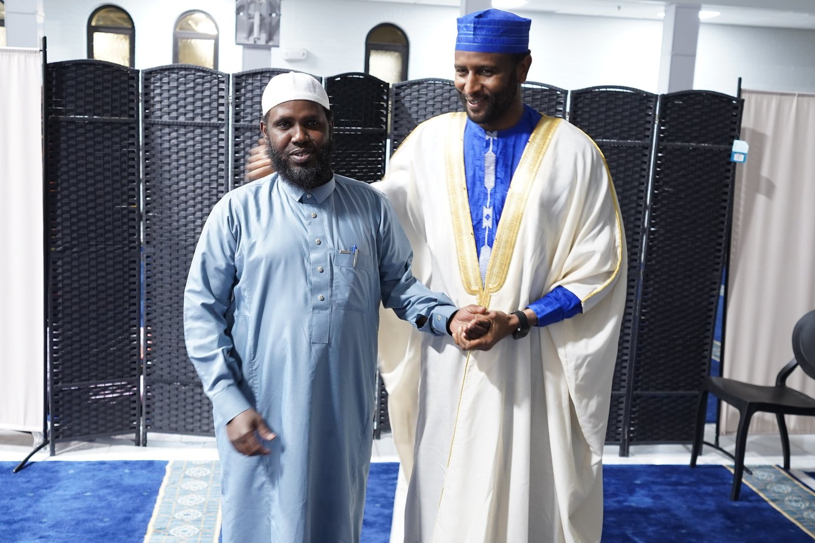 Dr. Adam Hilow standing beside a guest in a blue cap and cream robe with gold trim
