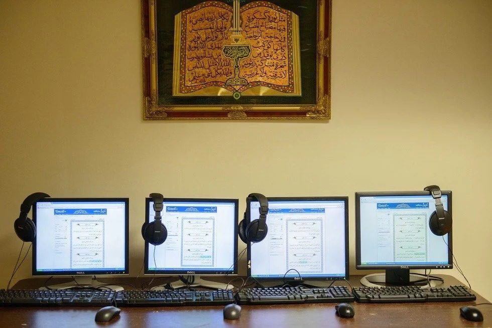 Computer lab with Qur'an software open on the monitors beneath a framed calligraphy